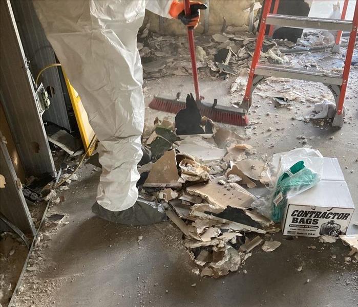 SERVPRO technician in a white tyvek suit sweeps up a pile of debris from fire damage.