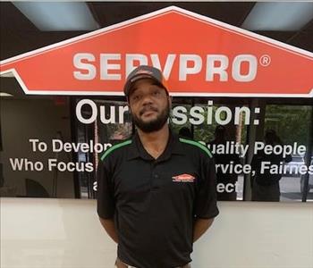 Corey in front of our SERVPRO mission sign, wearing a black SERVPRO polo and SERVPRO hat.