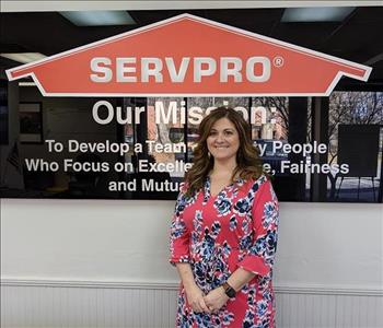 Rachel in front of the SERVPRO mission statement sign. Wearing a red and blue floral dress.