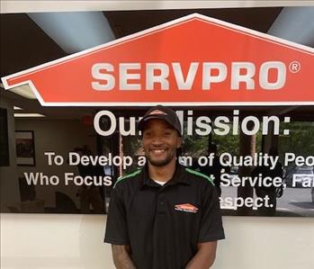 Lonnie in front of our SERVPRO mission sign, wearing a black SERVPRO polo and SERVPRO hat.