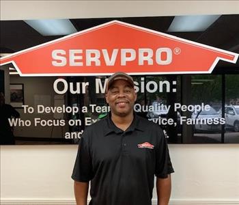 Antonio in front of our mission statement SERVPRO sign. Antonio is wearing a black SERVPRO polo and SERVPRO hat.