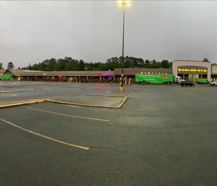 Three green servpro tractor trailers parked in a retail parking lot after flood damage.  Golds Gym sign is visible. 
